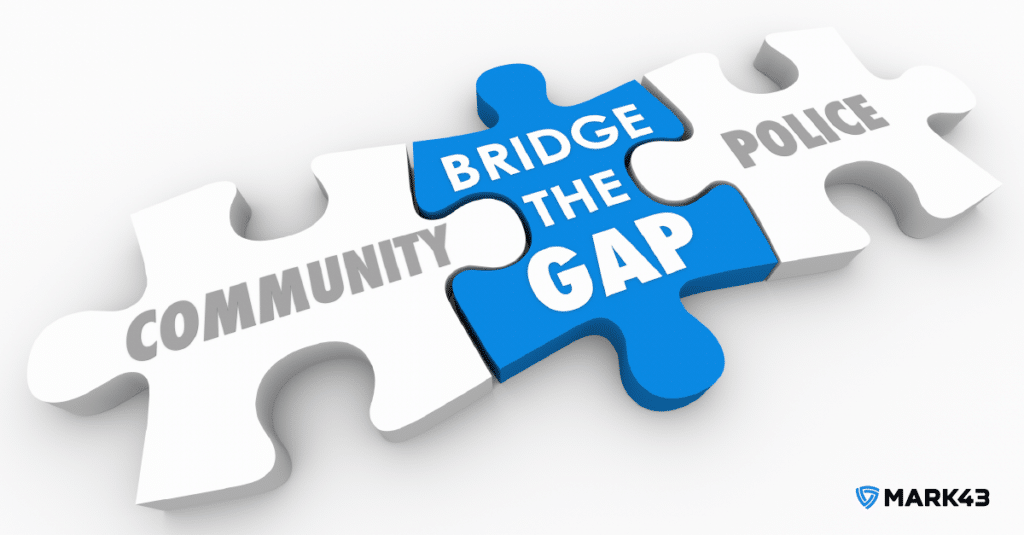Three puzzle pieces in a row. The puzzle piece on the left says “community.” The puzzle piece on the right says “police.” The puzzle piece in the middle, which connects the left and right puzzle pieces together, says “bridge the gap.”