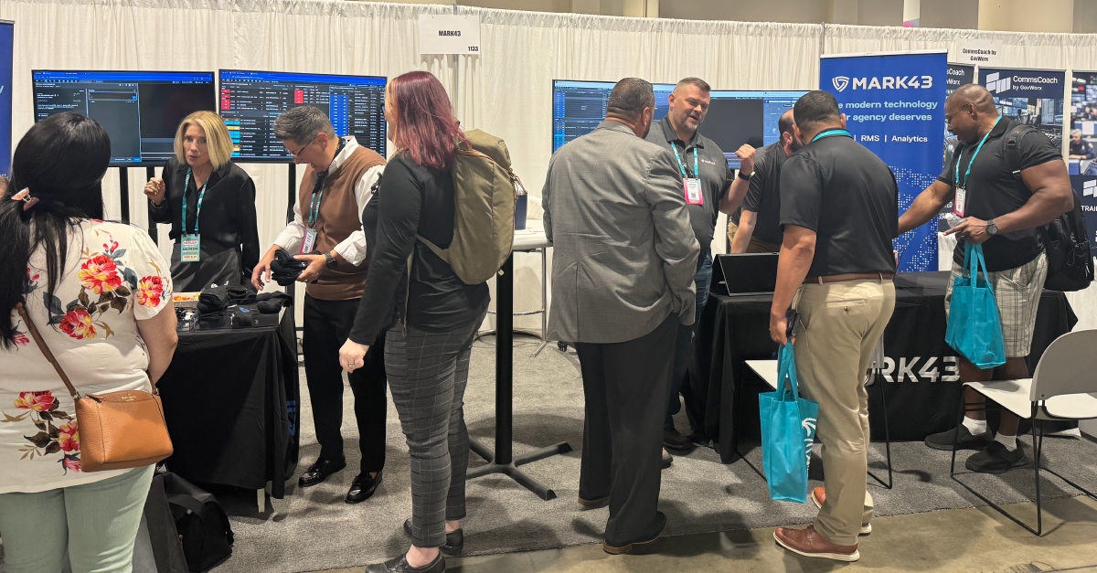 People interacting at a Mark43 booth with multiple computer screens at a technology conference or trade show.