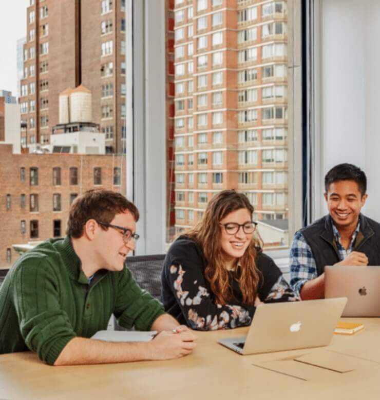 3 co-workers smiling while in conference room while looking at their laptops