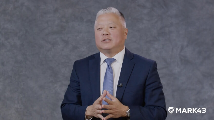 Businessman in a suit giving a speech with a Mark43 logo in the corner.