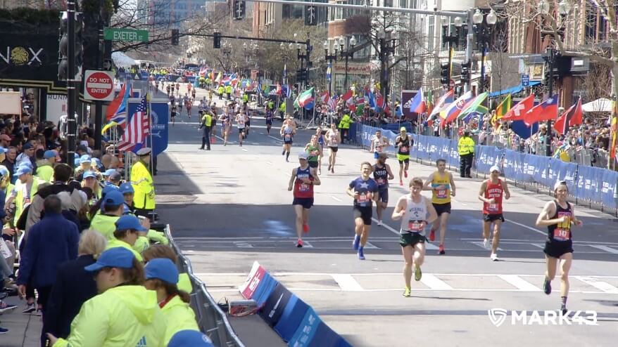 Marathon runners nearing the finish line with cheering crowds and international flags along the route