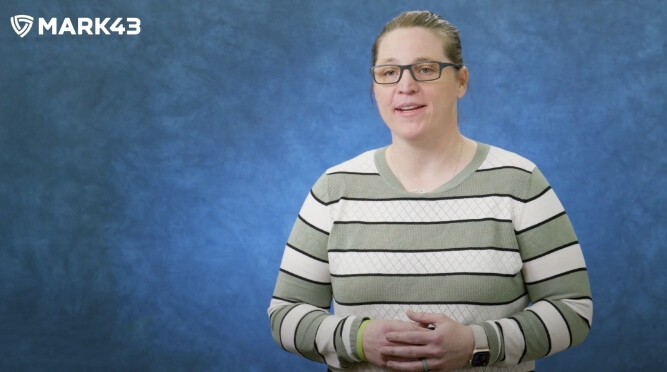 A person wearing glasses and a striped sweater, speaking in front of a blue background with a Mark43 logo.