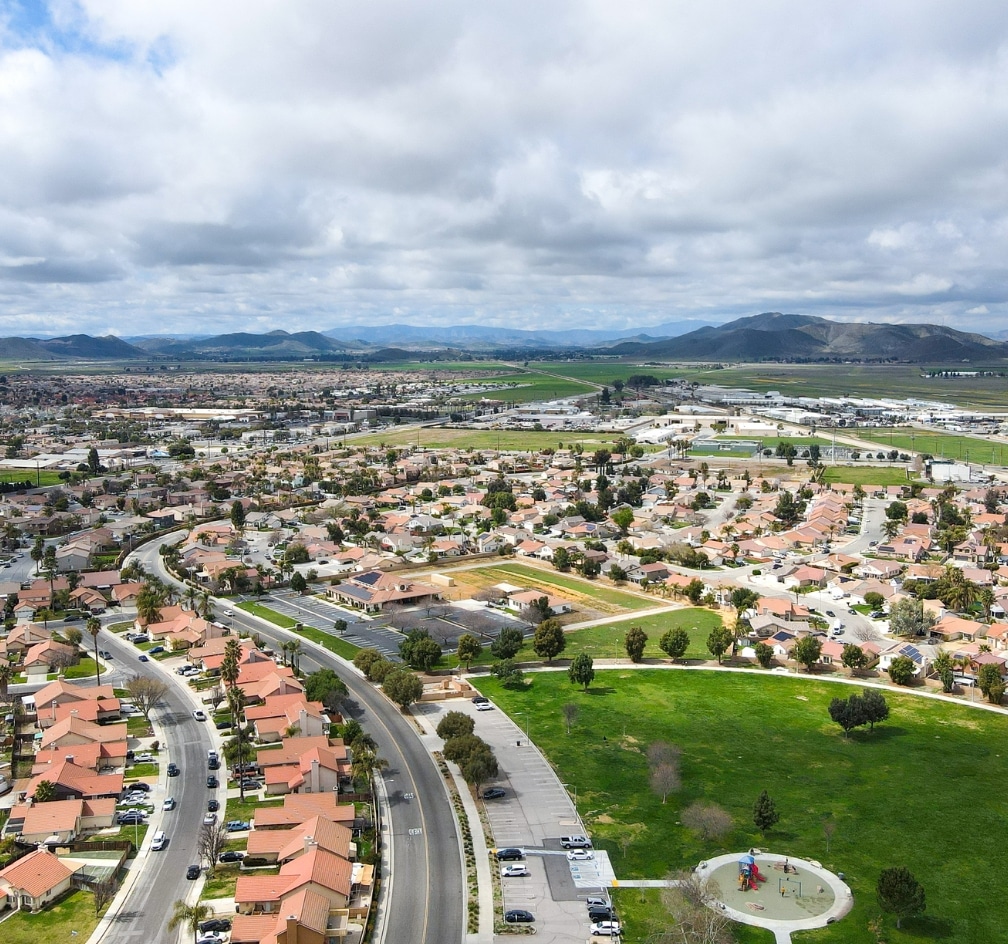 Aerial view of a suburban neighborhood with winding roads, houses, green spaces, and mountains