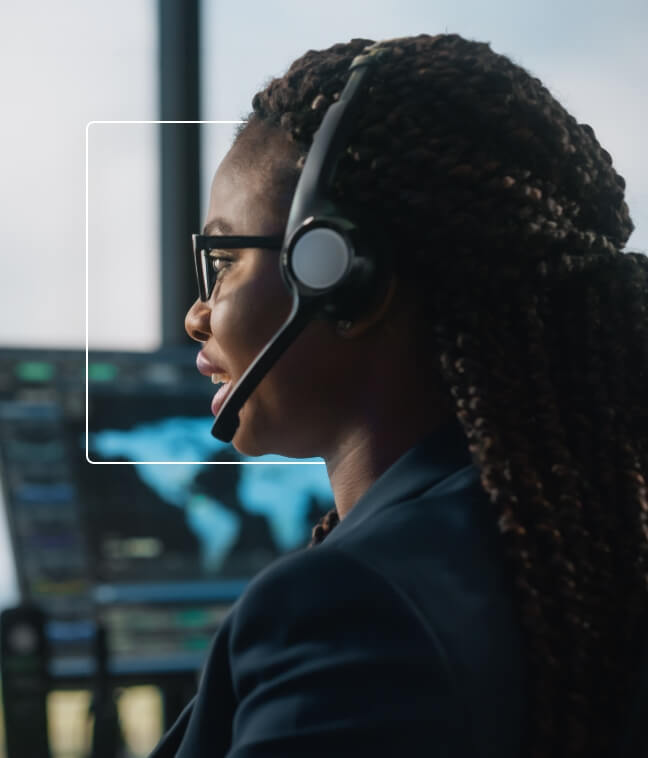 Dispatcher wearing a headset and glasses, working in a control room with screens in the background.