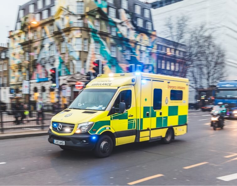 Yellow and green emergency ambulance with flashing lights driving through a city street