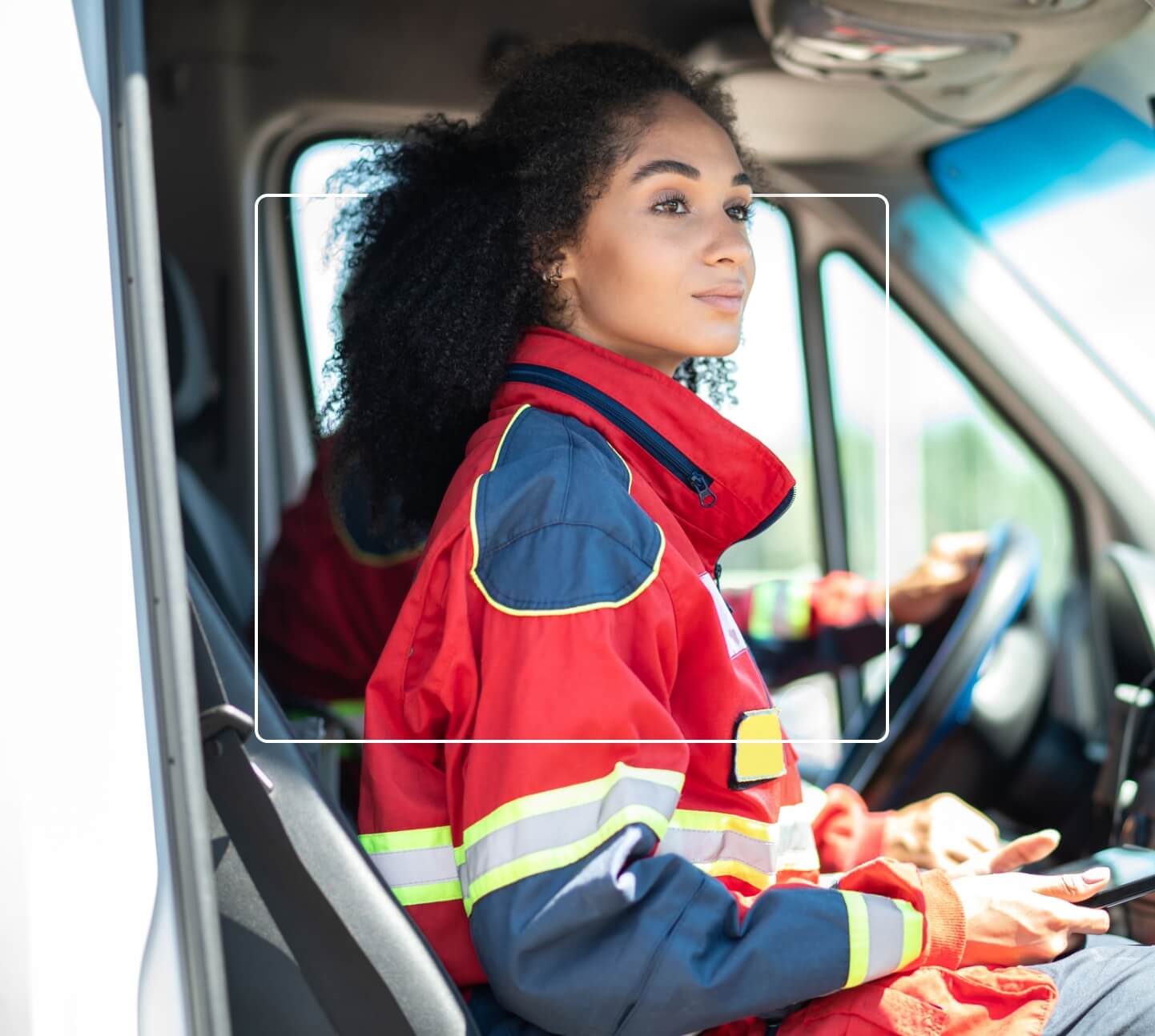 EMS responder seated with partner, looking out of vehicle on a sunny day