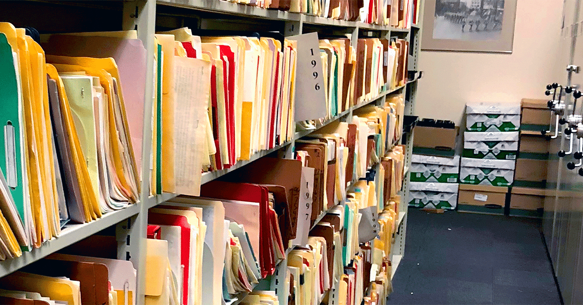 A photo of shelves filled with organized file folders, labeled by year, in an archive or records room.